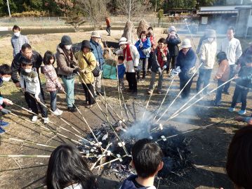 とんど焼きの場所にもどると、すっかり燃えてしまっていました。参加者の皆さんが、メダケを燃え残りの方に差し出していますが、何をしているのでしょうか。